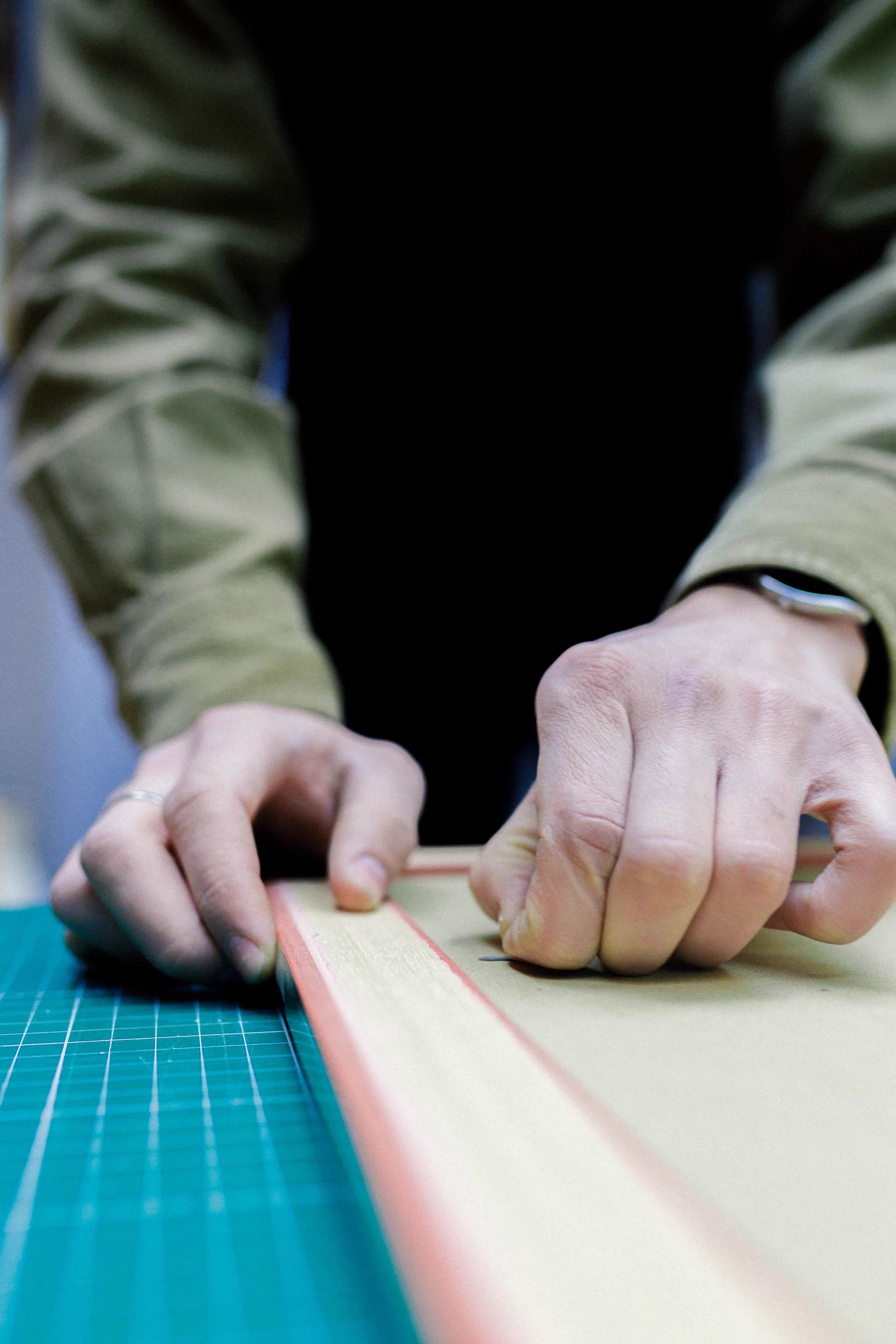 Hands holding a steel ruler against paper on a teal cutting mat, lining up a cut